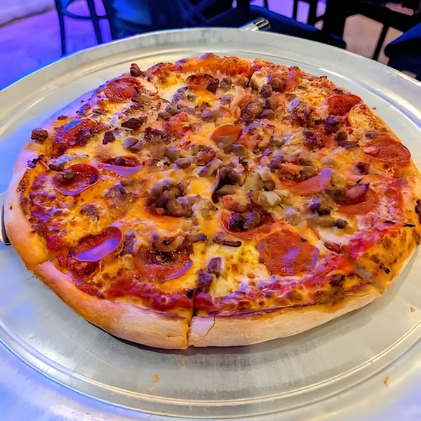 A whole Bruno's Pizzeria meat lover's pizza with pepperoni and sausage on a metal tray.