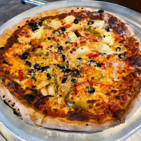A whole Bruno's Pizzeria pizza with pineapple, black olives, and bell peppers on a metal tray.
