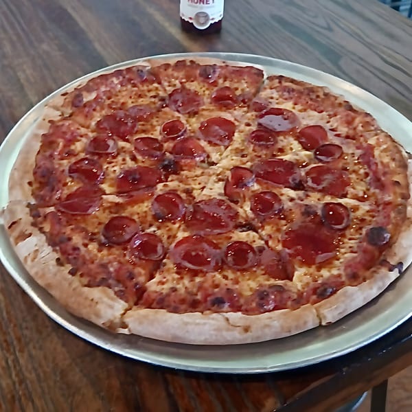 A whole pepperoni pizza from Bruno's Pizzeria on a metal tray, with a honey bottle in the background.